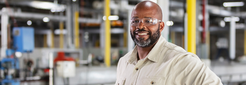 A man wearing safety glasses smiling inside of a factory